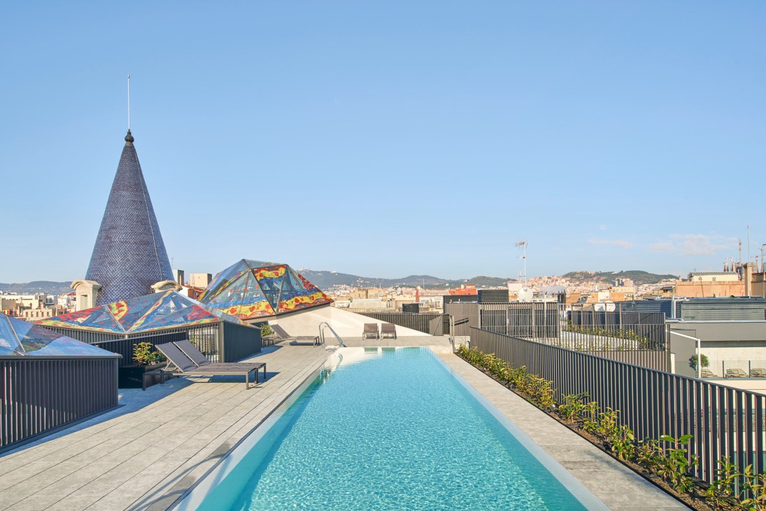 Rooftop pool and recreational area of Casa Burés with colorful architectural installations overlooking Barcelona cityscape.