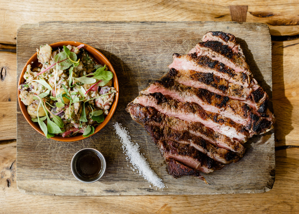 Sliced grilled meat and a salad served on a wooden board at CBD Provisions.