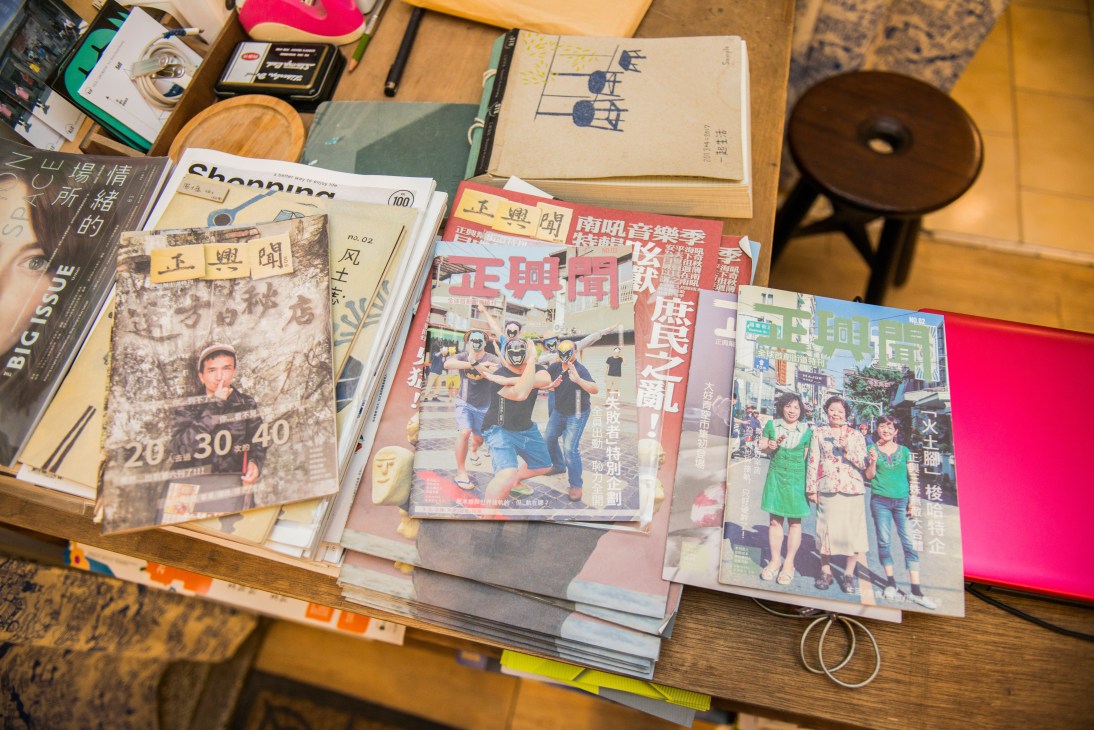 A wooden desk displays magazines and books with Chinese characters, including Zhengxing magazine, alongside vintage items and decorative objects.