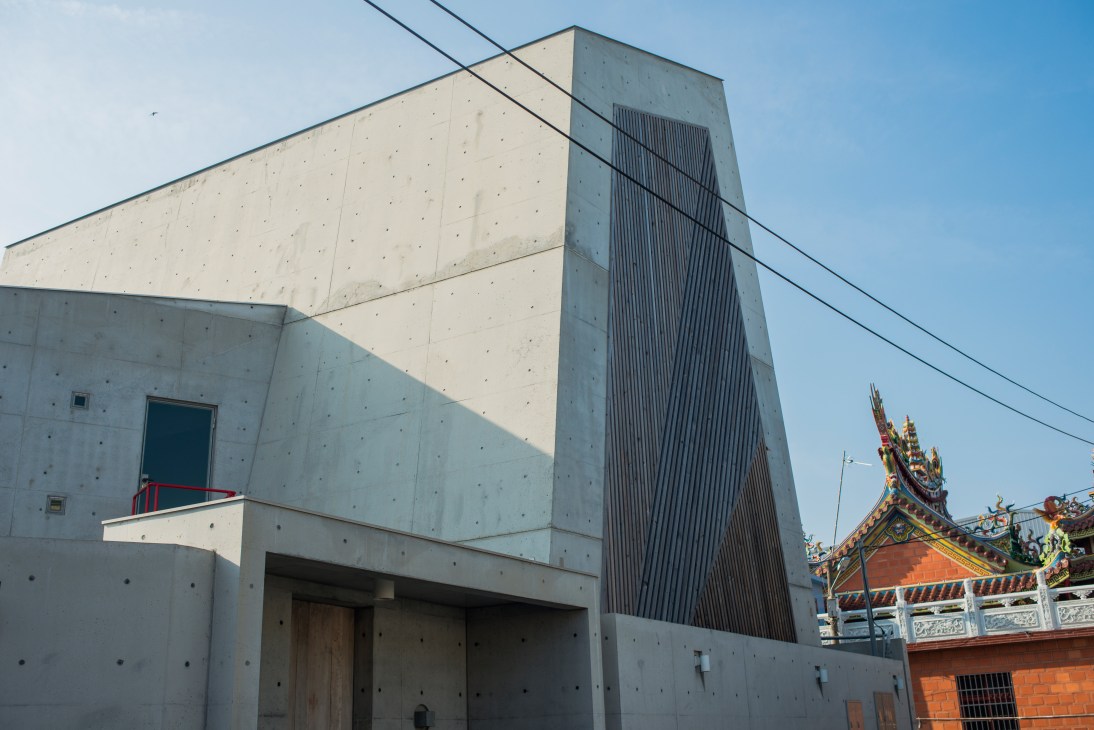 Concrete modernist guesthouse with geometric design next to ornate Asian temple in Tainan.