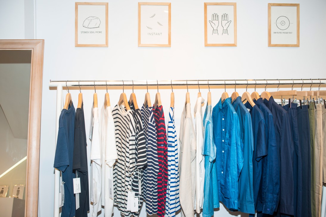 Interior of Washida clothing shop displaying striped shirts and blue jackets on wooden hangers with framed line drawings on white wall above.