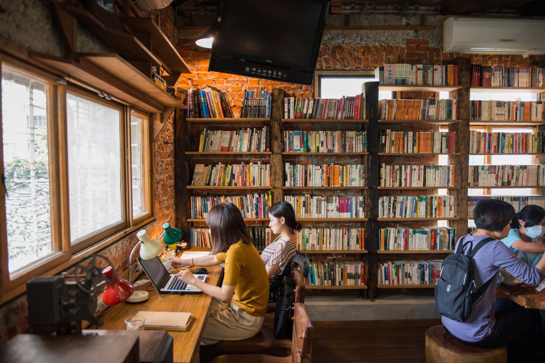 Woman working on laptop in Room A, a reading room with floor-to-ceiling bookshelves and exposed brick walls in Tainan.