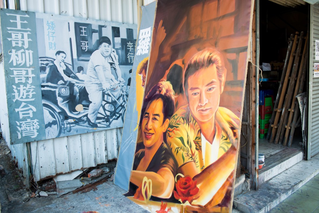Painted movie poster displayed outside Chin Men Theatre in Tainan featuring three men in colorful clothing with a red rose.