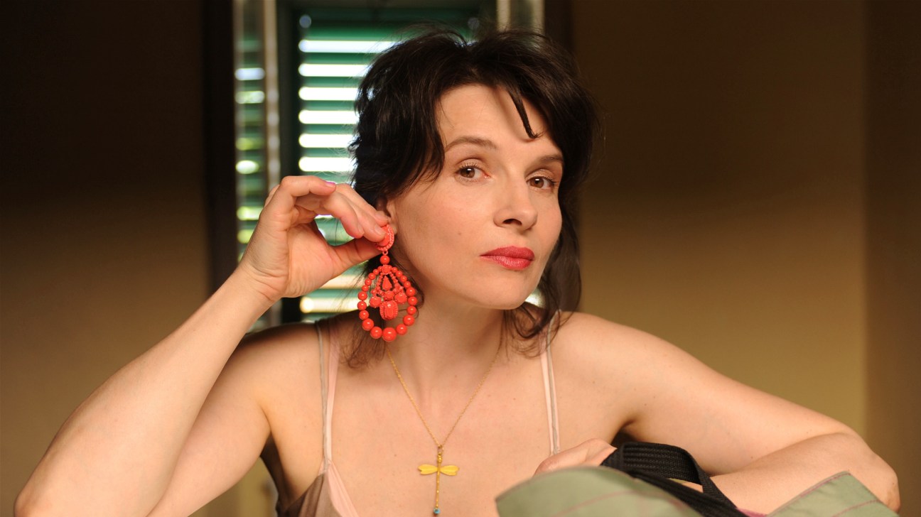 Woman with dark hair wearing red beaded earrings and a cross necklace looks pensively to the side.