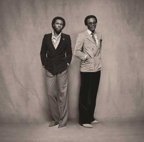 Two men in 1970s-style suits posing against a neutral backdrop.