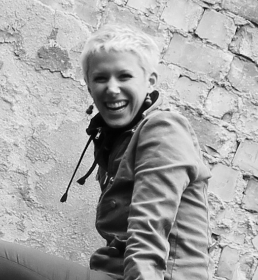Black and white portrait of Christine McLaren smiling against a textured brick wall.