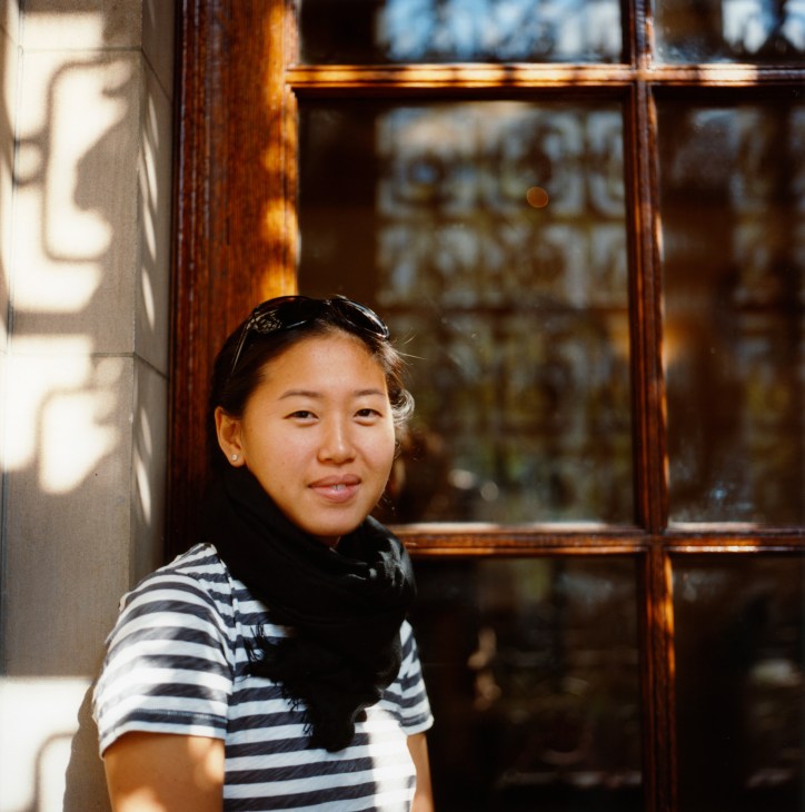 Young woman in striped shirt smiling at camera near wooden-framed window