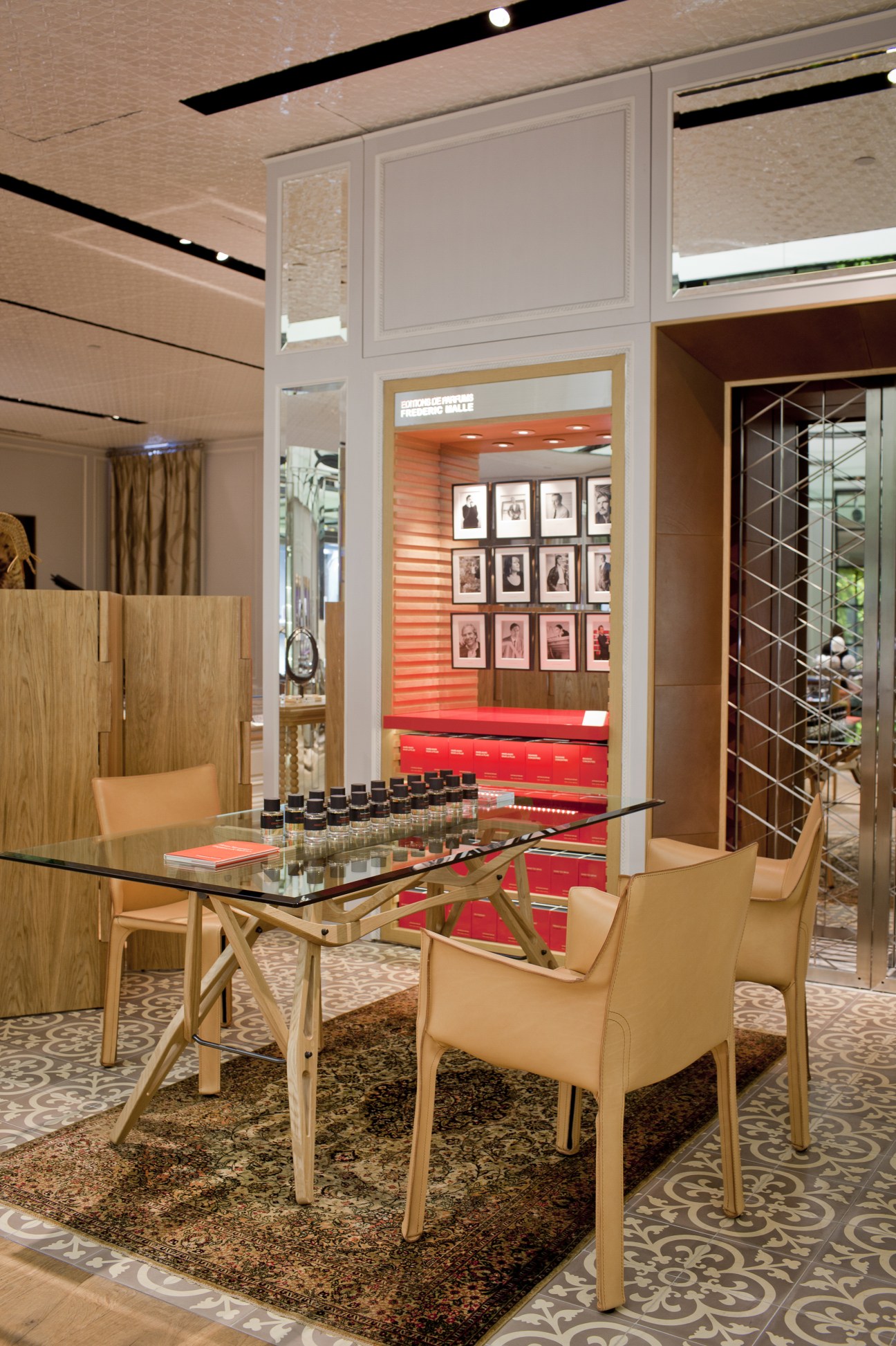 Modern luxury watch retailer interior with glass display table, cream chairs, and red accent wall featuring portrait photographs.