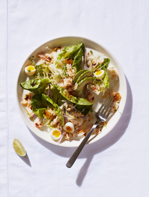 Crab and quail egg salad with avocado, fennel, lettuce, and crispy chilli oil on a white plate.