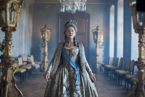 Helen Mirren as Catherine the Great in ornate 18th-century Russian imperial dress in a grand palace corridor.