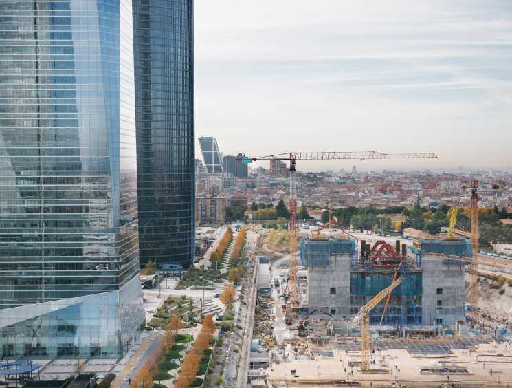 Madrid skyline with glass skyscrapers, construction cranes, and concrete building foundations under development.