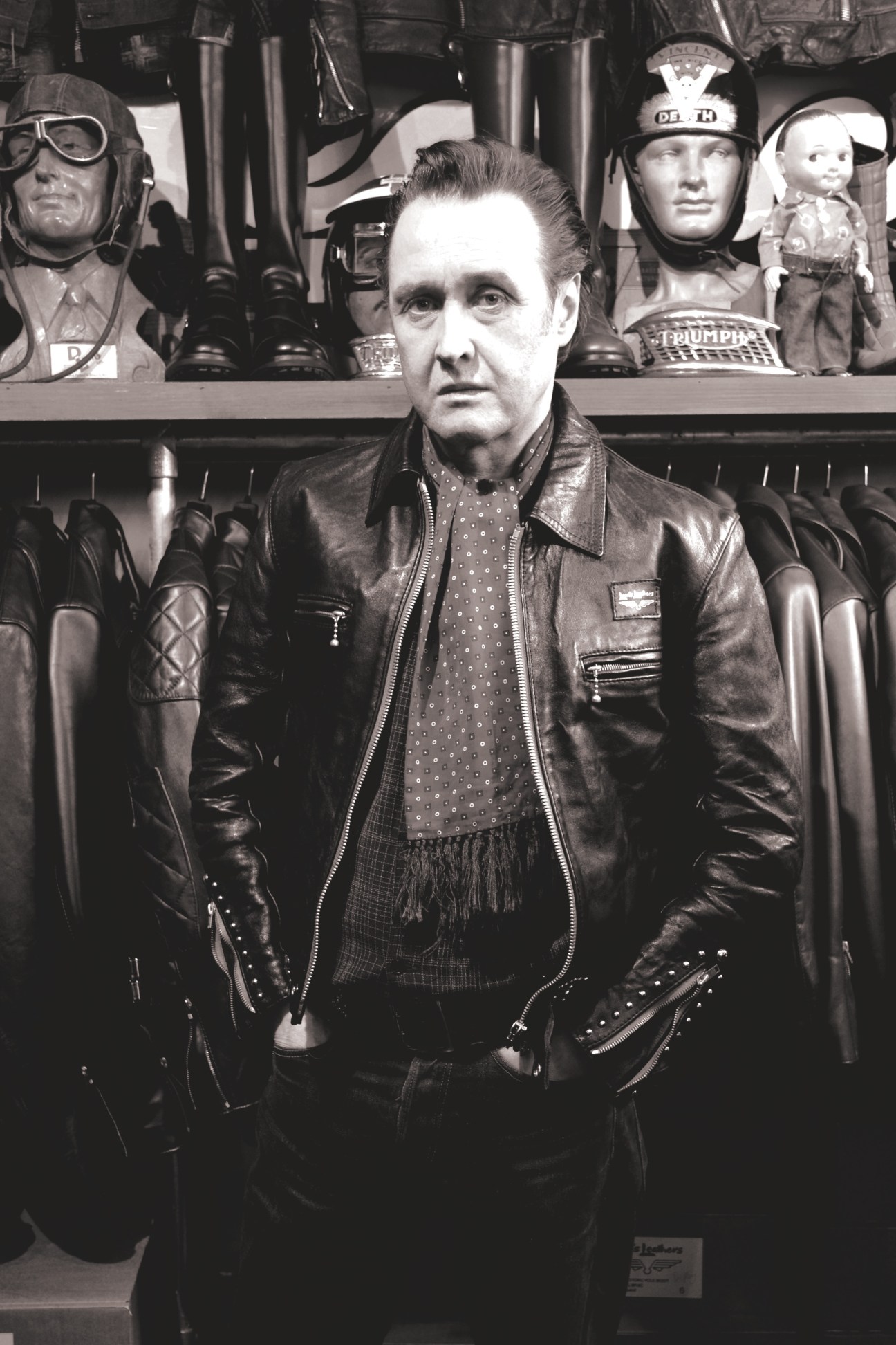 Derek Harris, proprietor of Lewis Leathers, standing in front of a display of black leather motorcycle jackets.
