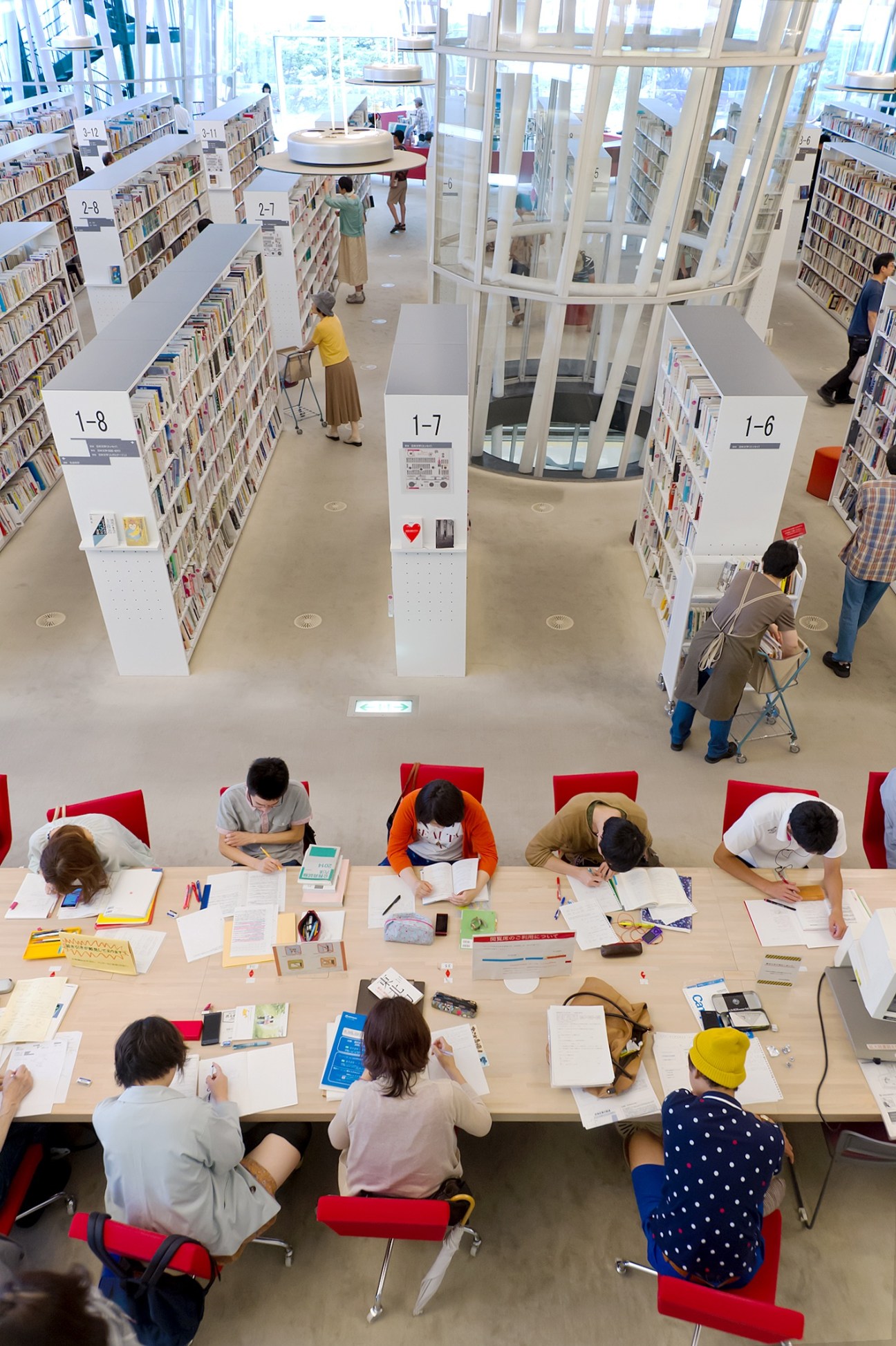 Overhead view of a modern library with people studying at tables surrounded by bookshelves.