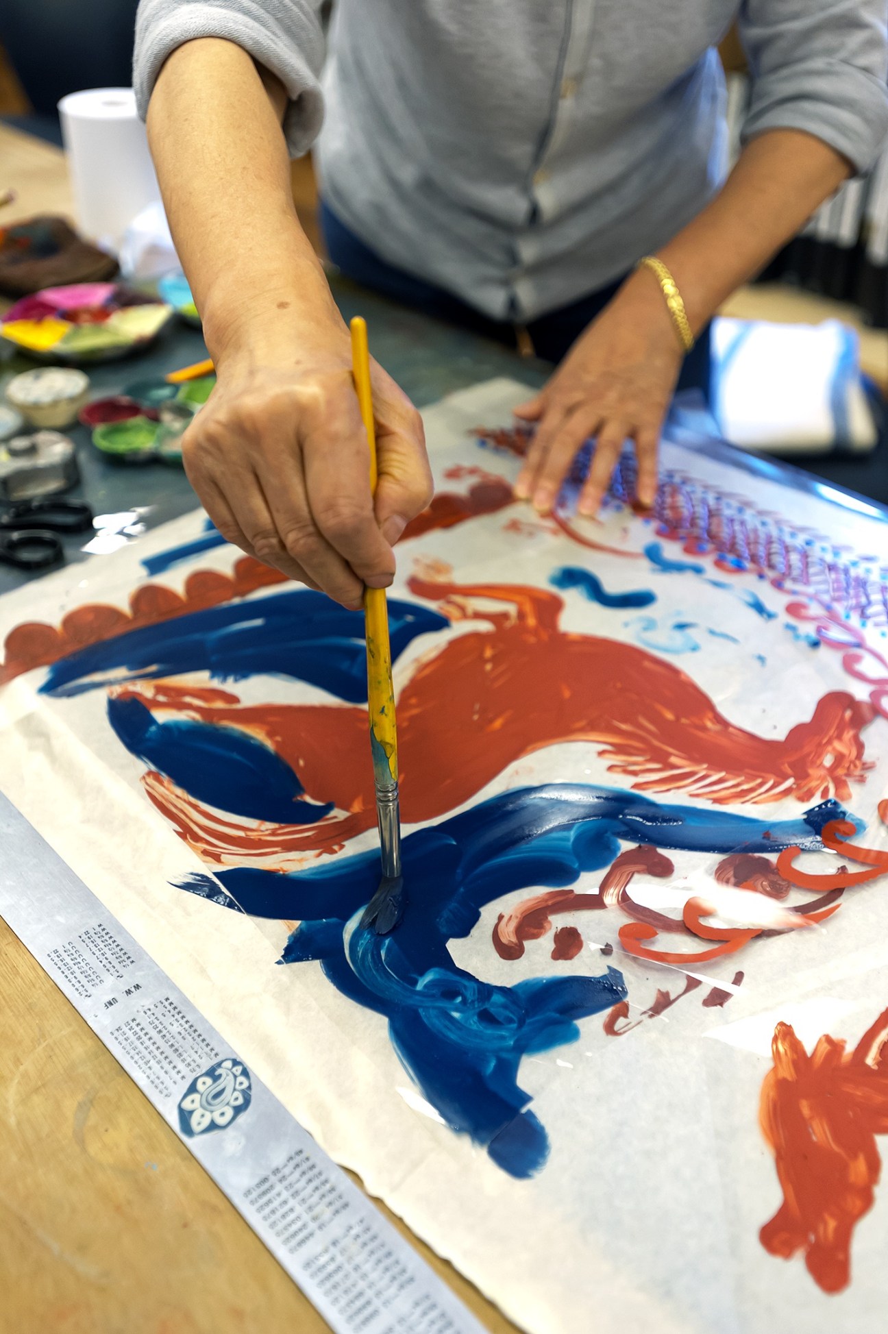 Designer painting colorful patterns on fabric with blue and red paint and a brush.
