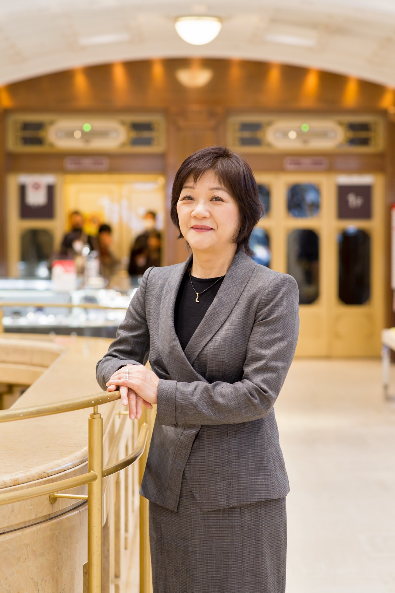Miharu Koezuka, senior marketing director at Takashimaya, stands in an elegant department store interior with gold fixtures.