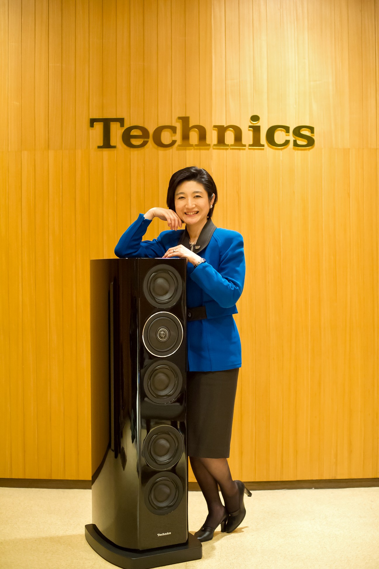 Michiko Ogawa, Director of Technics at Panasonic, posing with a tall black speaker against a yellow ribbed wall.
