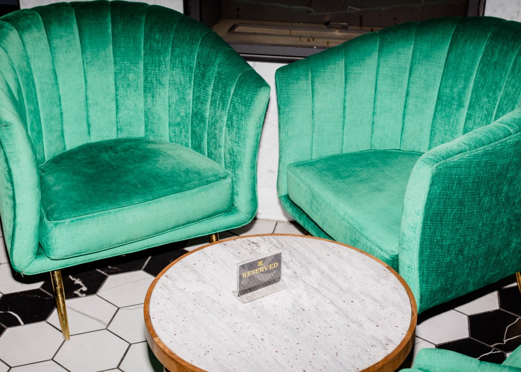 Two green velvet armchairs flanking a round marble table with a reserved sign at The Wild Detectives.