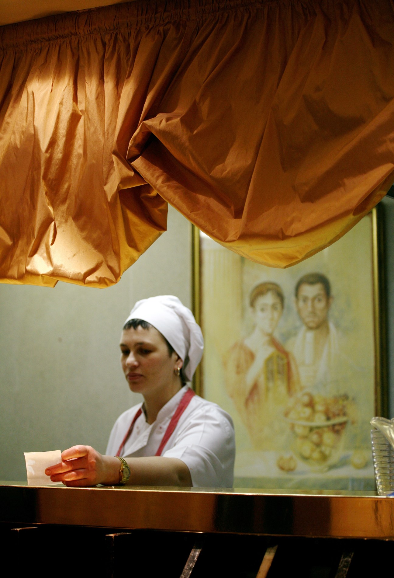 A staff member at Convivium restaurant's reception desk wearing a white head wrap and red sash.