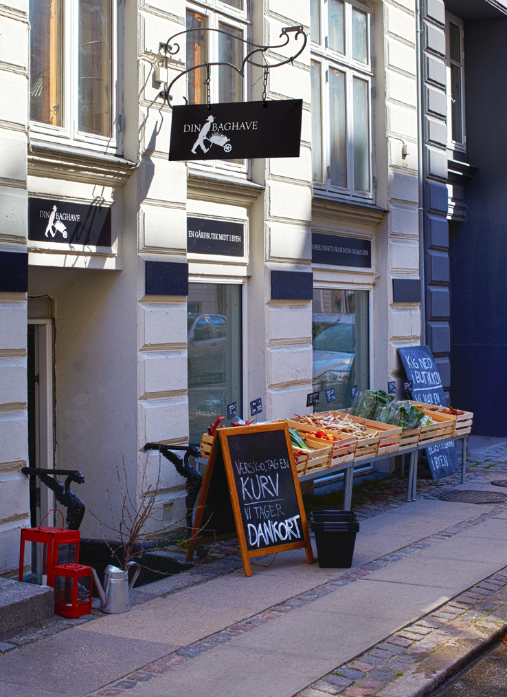 Din Baghave grocery storefront in Copenhagen with hanging sign, display of fresh produce in wooden crates outside.