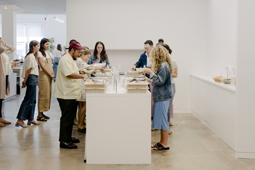 Staff members gather around a white table at Warby Parker's Manhattan headquarters for a catered Tuesday lunch.