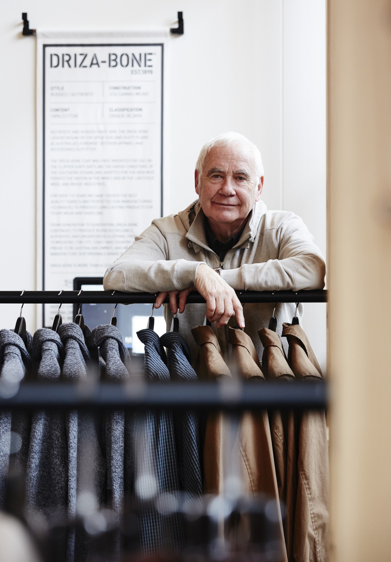 Stephen Bennett, creative director of Driza-Bone, posing with outerwear products displayed below a brand sign.