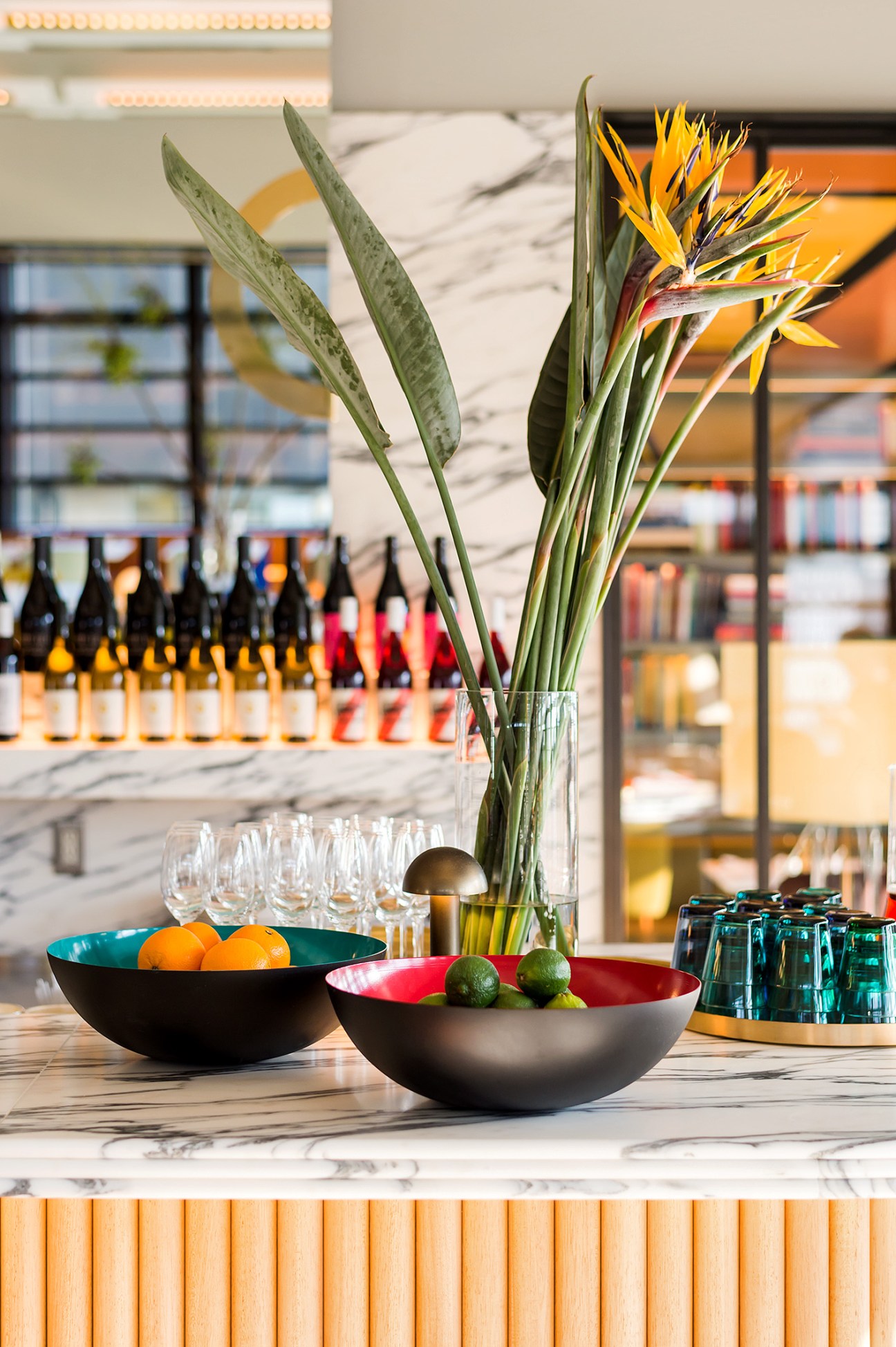 Modern bar counter with bird of paradise flowers, bowls of fruit, and glassware.