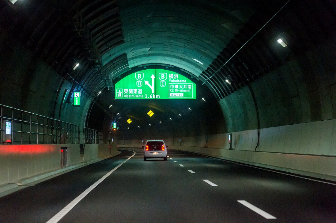 Car driving through Tokyo's Yamate Tunnel with green directional signs overhead.