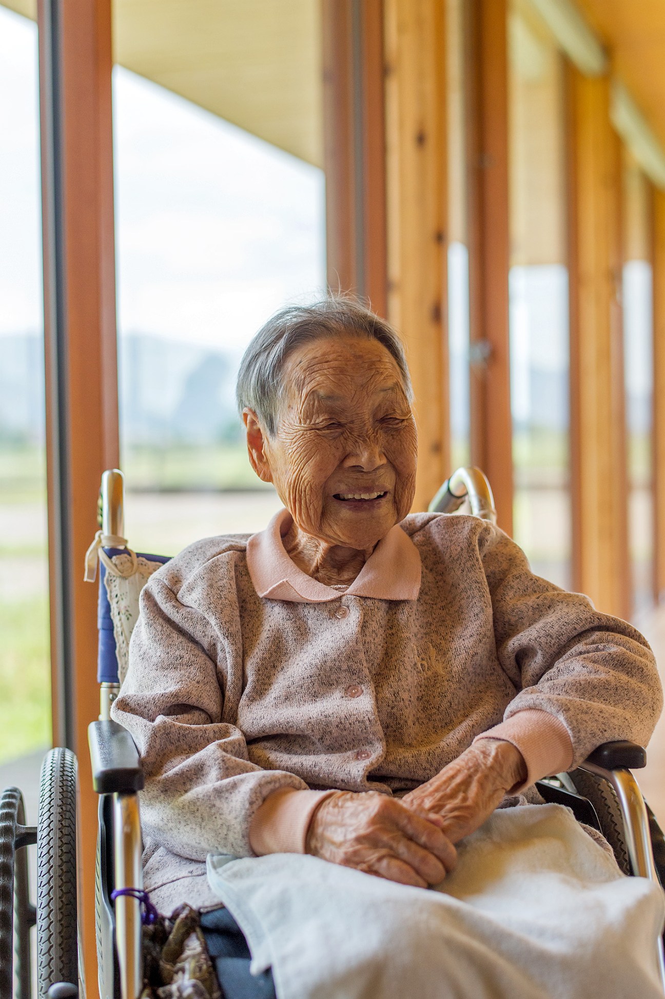 Elderly resident Suekiku Sugimoto, 102, smiles by a large window overlooking rice paddies at Ebino Ryofuen nursing home.