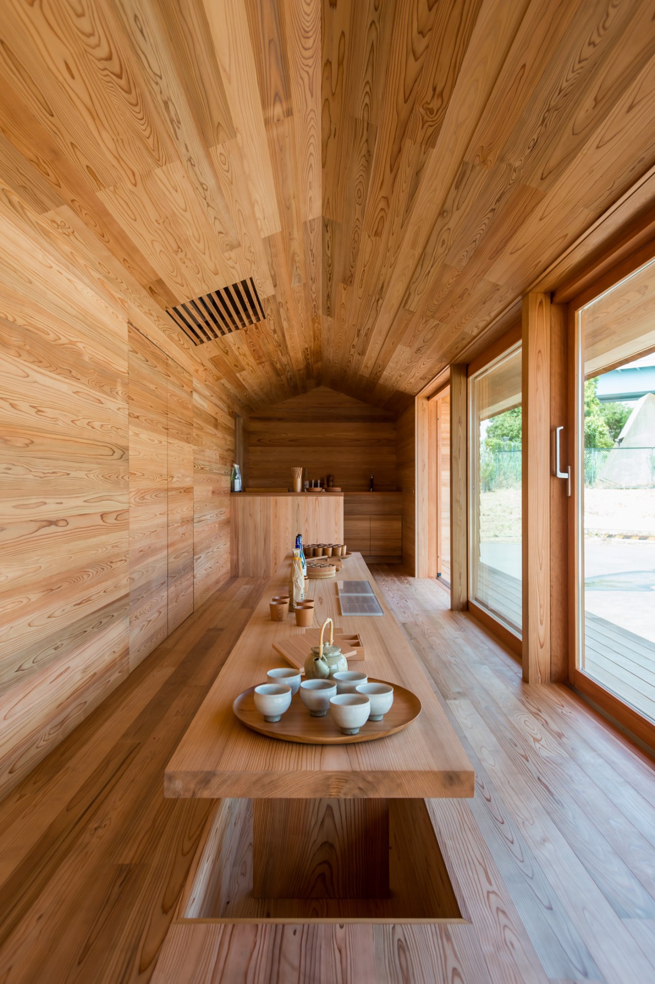 Interior of Yoshino-sugi Cedar House with wooden walls, ceiling, central table with ceramic vessels, and shelving.