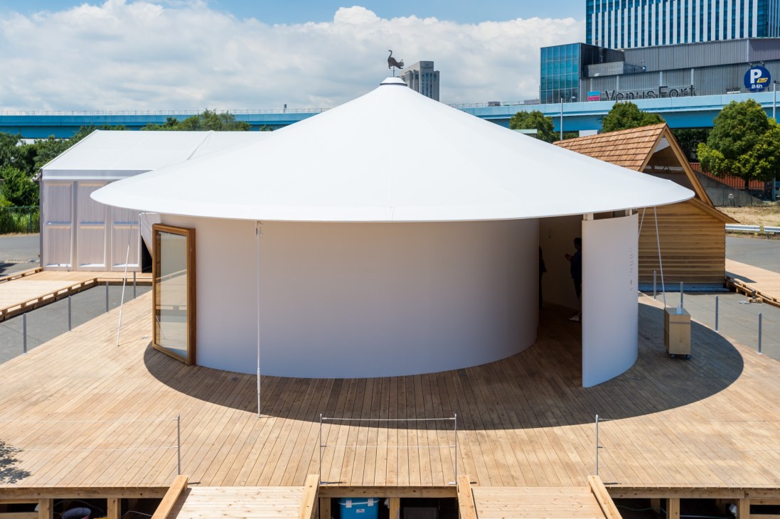 Hiragana-no Spiral House with white conical roof and curved walls on wooden deck by waterside.