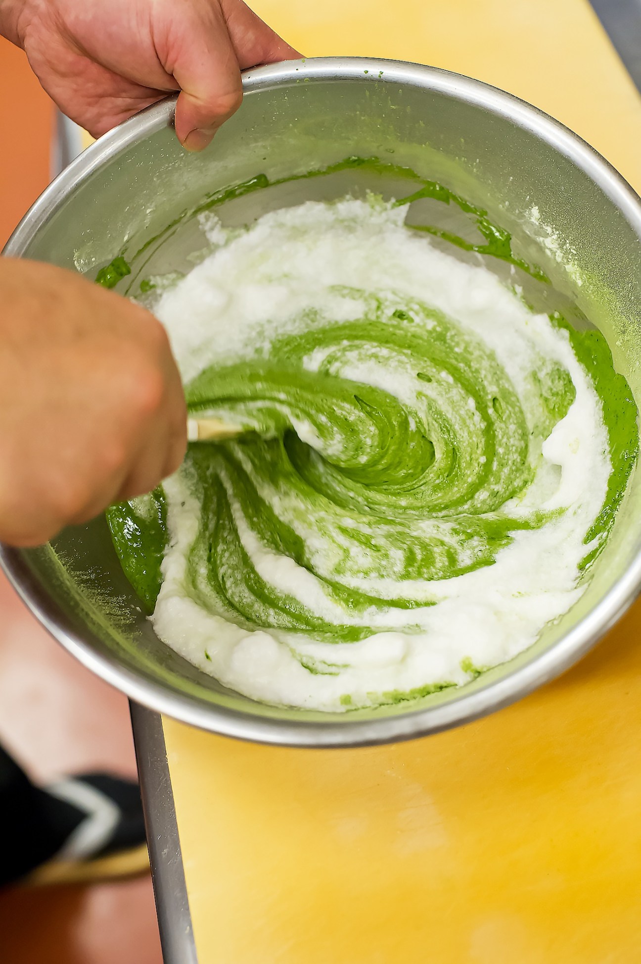 Hand holding a bowl of green tea cake batter with white and green swirled mixture.
