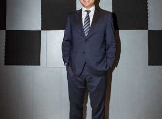 Man in navy suit standing in modern interior space with geometric wall panels.