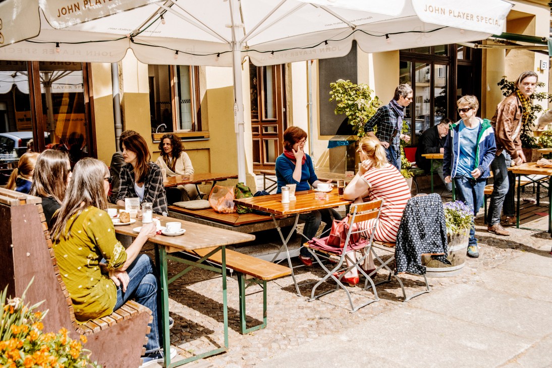 Outdoor biergarten seating in Berlin with wooden tables, benches and umbrellas where people gather.