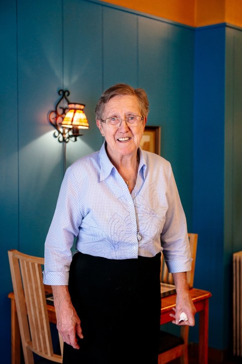Woman in blue checkered shirt and black skirt standing in colorful interior with teal walls and orange ceiling.