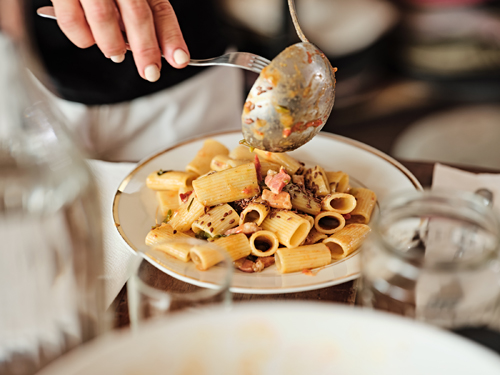 Hand holding a spoon of pasta with peppers and rigatino over a plate of pasta at Reinhard Plank in Florence.
