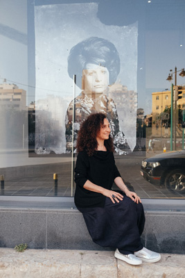 Woman sitting in front of a large portrait artwork displayed on a building facade in Beirut.