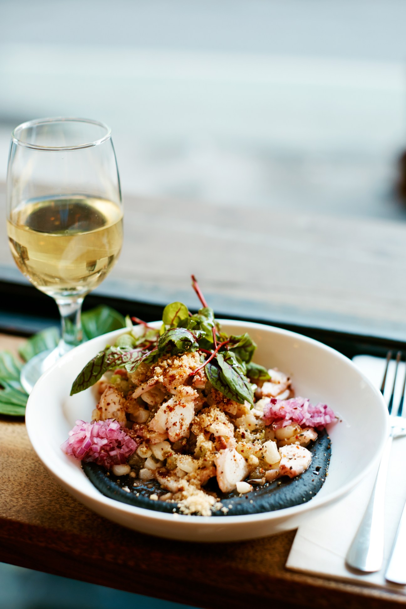 Octopus and hominy salad with black bean puree served on a white plate with white wine.