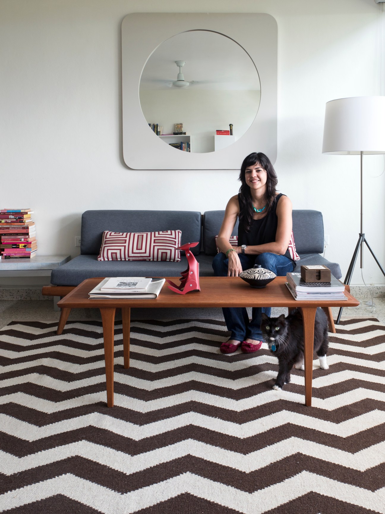 Journalist Laura Perez sits on a mid-century sofa in her El Monte apartment with her cat beside her.