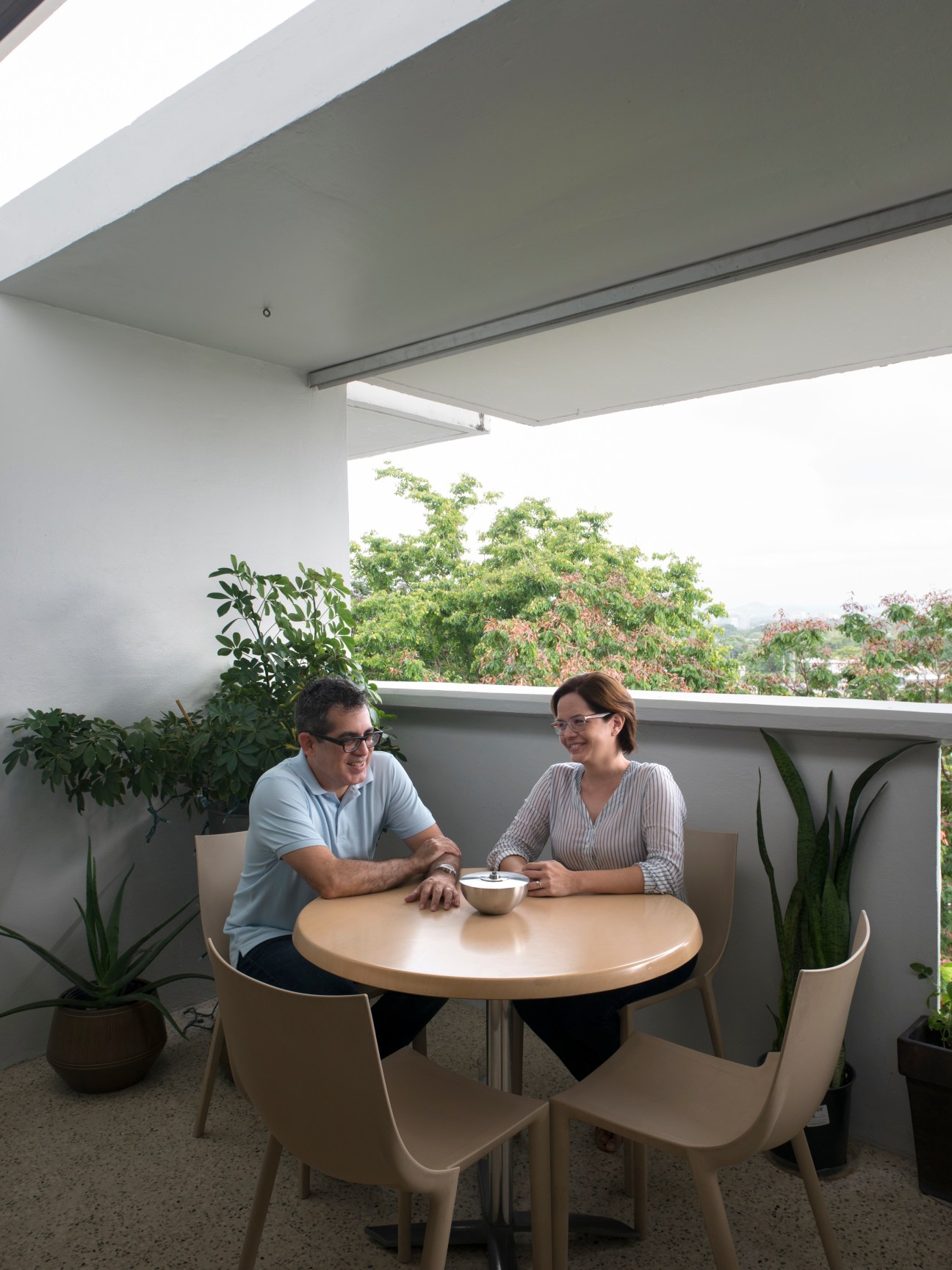 Two architects sit at a round table on a modernist balcony overlooking tropical gardens at El Monte.