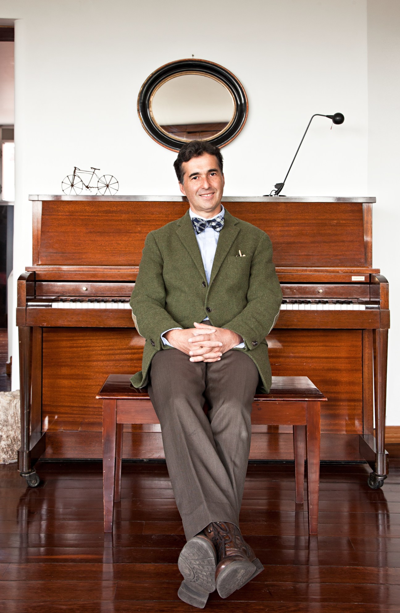 Portrait of architect Enrique Uribe sitting at a wooden piano in his Park Towers apartment.