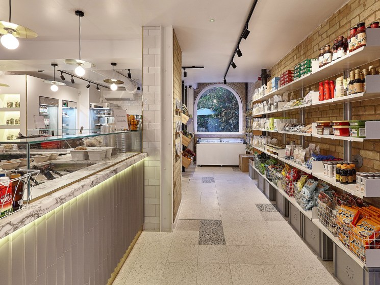 Interior of Mee Market in London showing deli counter on left and shelving with products on right brick wall.