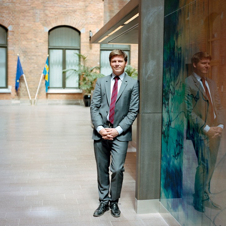 Erik Ullenhag, Sweden's Minister for Integration, standing in an office courtyard with flags in the background.