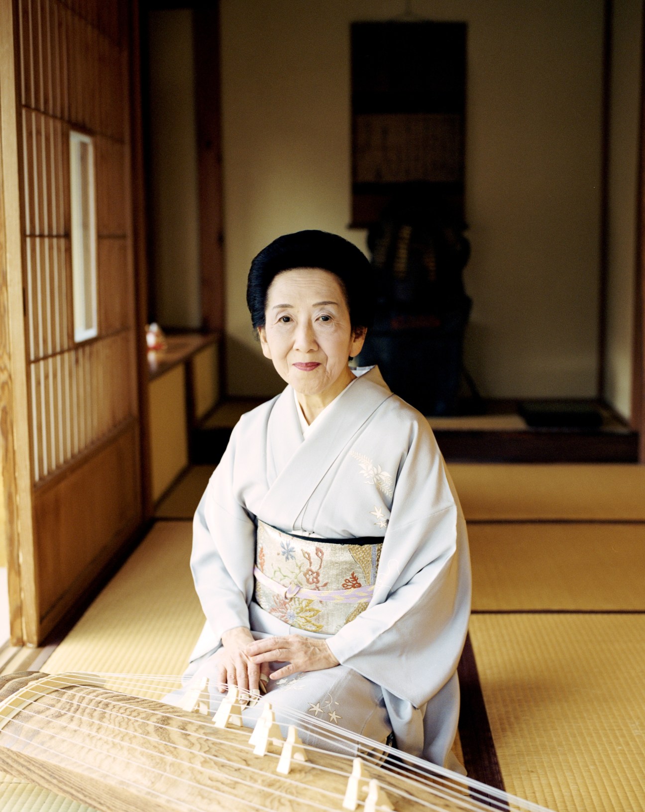 Shoin Yamase VI, a koto player in traditional dress, sits with the 13-stringed instrument in a Japanese tatami room.