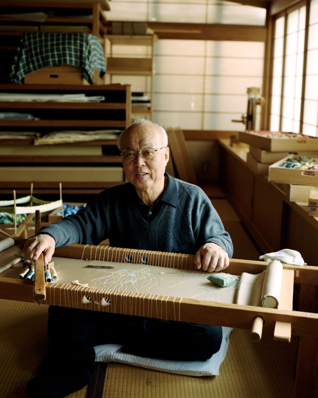 Kiju Fukuda, an elderly Japanese embroiderer, sits at his work table surrounded by silk threads in his Kyoto studio.