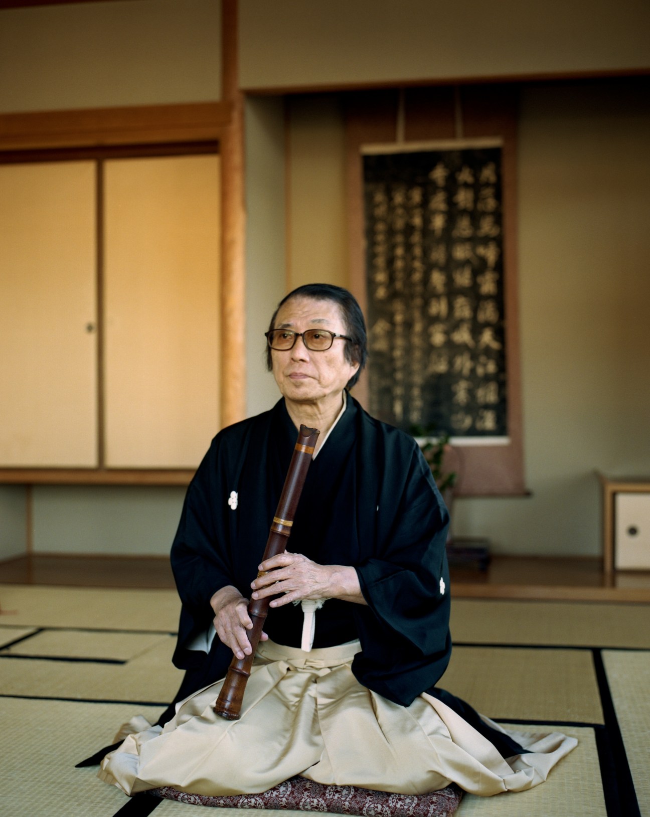 Hozan Yamamoto, shakuhachi player, seated on tatami mat holding bamboo flute in traditional Japanese room.