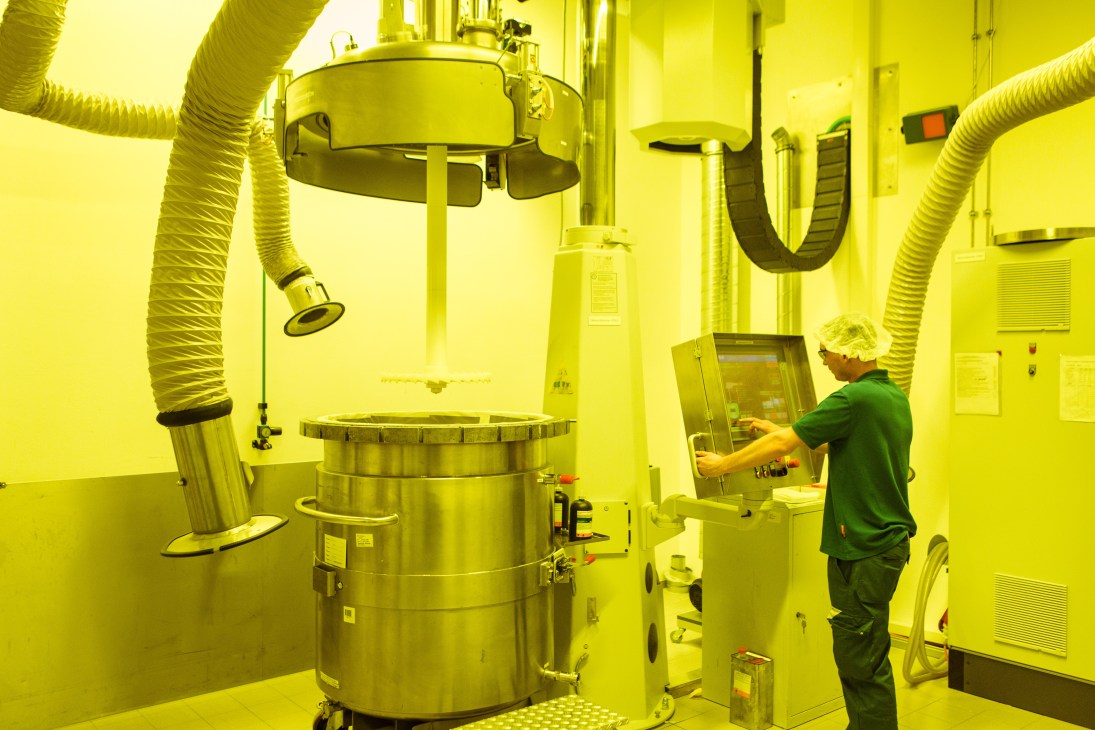 Worker in green uniform operates industrial adhesive manufacturing equipment in bright yellow facility.
