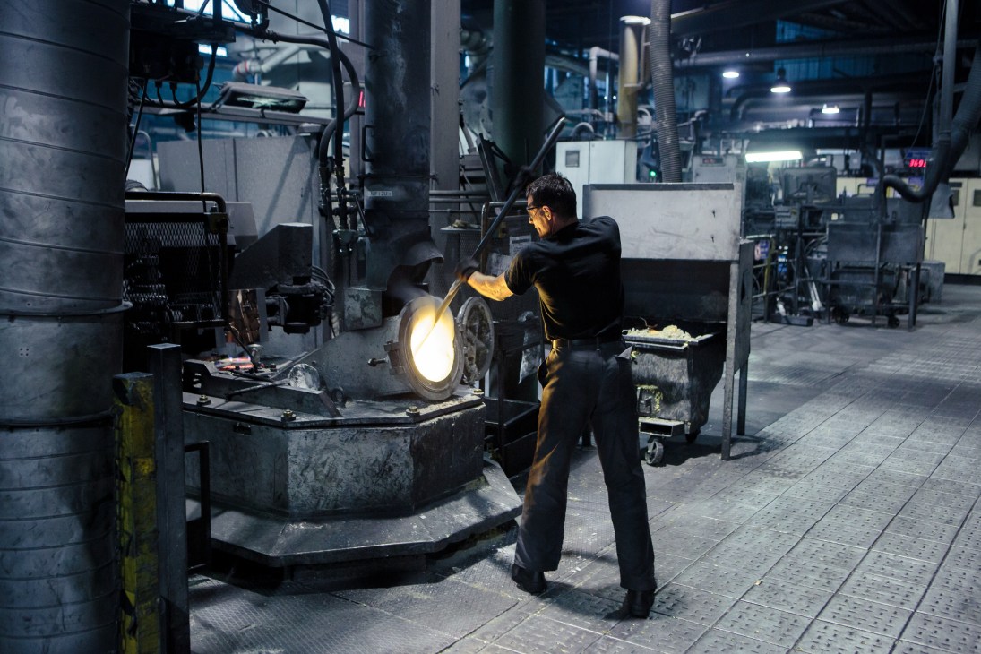 Worker inspects industrial manufacturing equipment in a factory facility with machinery and overhead lighting.