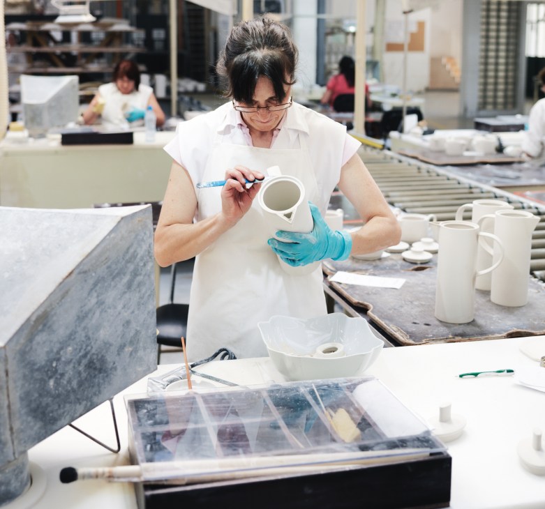 A woman in protective gloves hand-finishes a white porcelain piece at Vista Alegre factory.