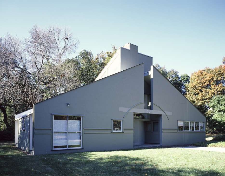 Modernist house with angular grey facade and geometric forms surrounded by autumn trees.