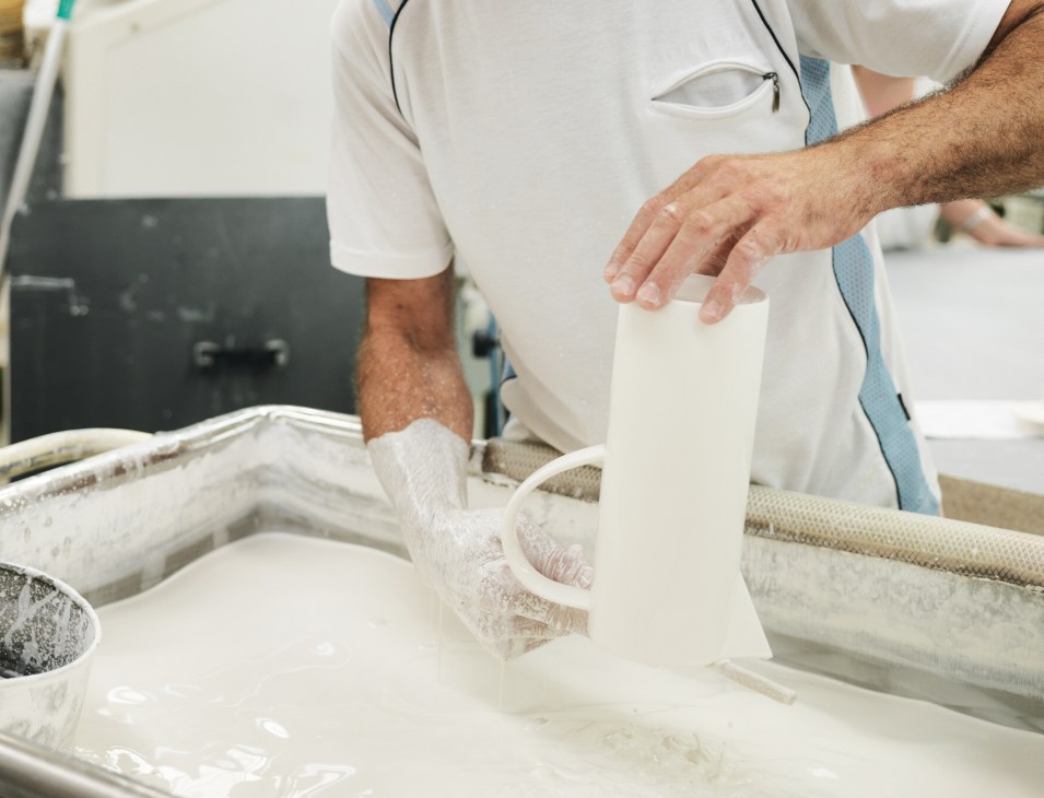 Worker hand-glazing a white porcelain coffee pot by dipping it into milky glaze mixture.